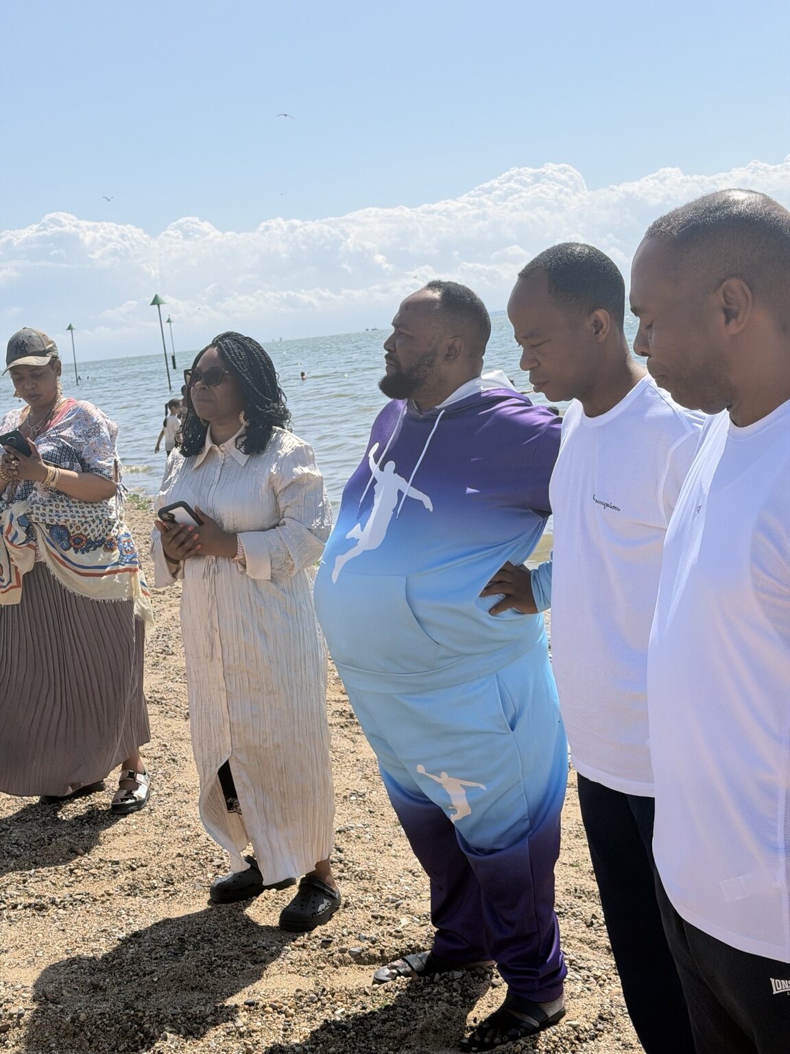 Pastor Andre Salazaku praying with baptism candidates by the sea